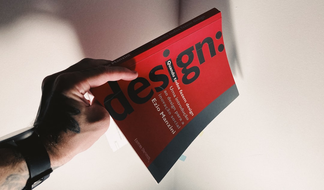 Main tatouée tenant un livre rouge consacré au design.